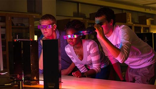 three students view a laser in a dark classroom