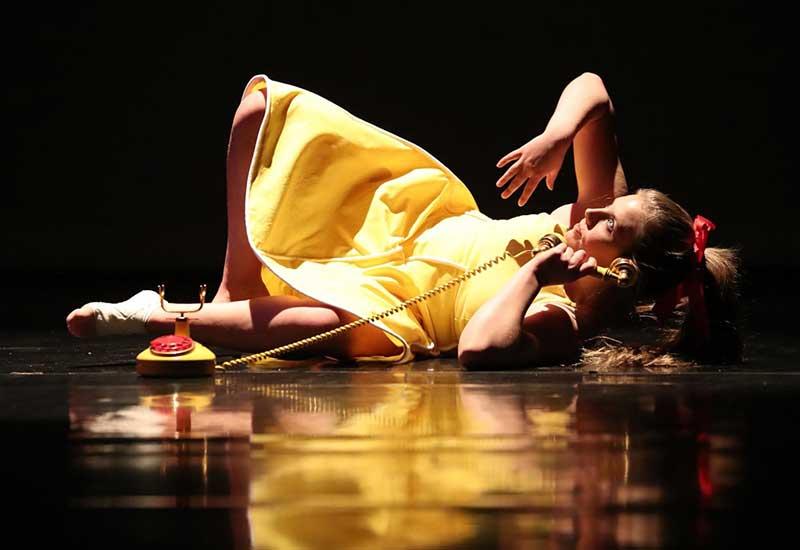 在一场舞蹈演唱会上，一名身穿黄色连衣裙的表演者拿着手机躺在舞台上