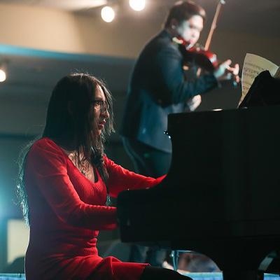 在FAME才艺表演中，一名身穿红色连衣裙的女子正在弹钢琴