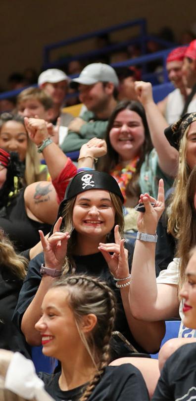 一群体育菠菜大平台学生微笑着欢呼，中间是一名戴着海盗帽的女子在抛舞