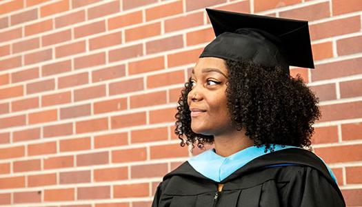 一个戴着毕业帽和毕业礼服的女人站在砖墙前