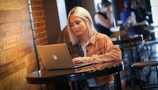 一位女士坐在咖啡店的桌子旁，手里拿着她的笔记本电脑
